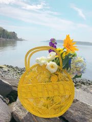 Primrose Yellow 100 % Handwoven, Iraca Palm Bag with “Sagharbor” Woven Across Front on beach with flowers